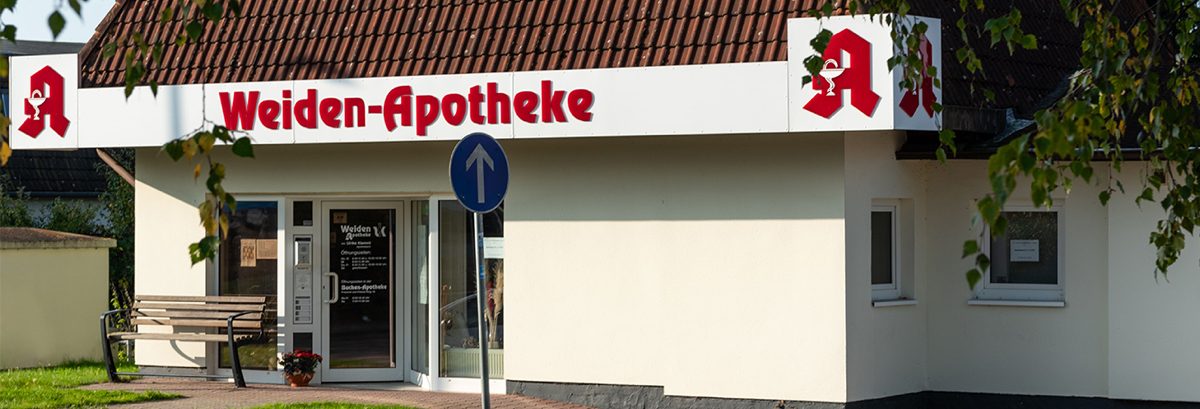 Außenansicht der Weiden-Apotheke in Sanitz mit Eingang, Apotheke-Schriftzug und rotem Apothekenzeichen auf weißem Hintergrund.